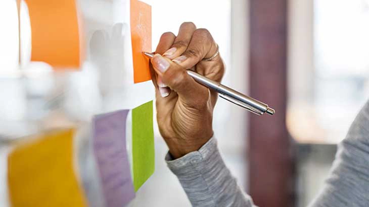 Close up view of hand writing on a orange post it note on a wall