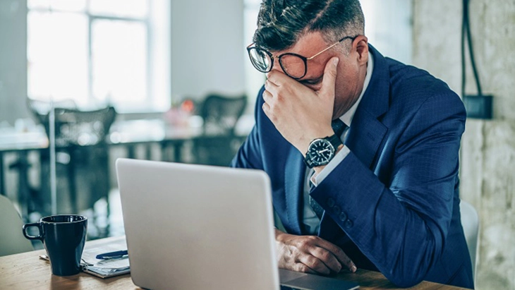 Man with elbows on desk and a hand covering face