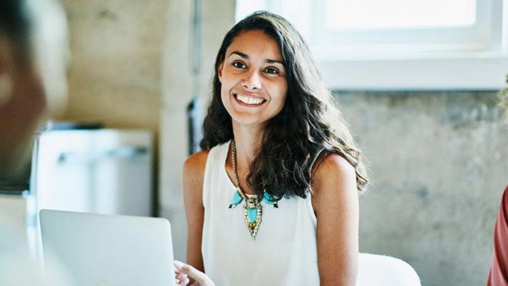 Woman in office using laptop and smiling