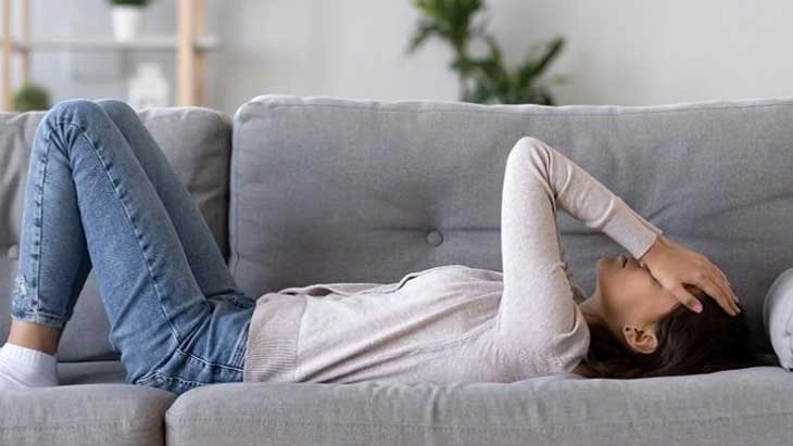 Woman lying down on couch with her hands over her eyes