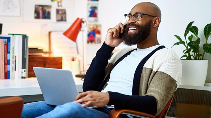 Man seated with laptop on his lap and talking on mobile