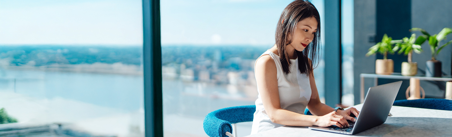 Professional working on a laptop in a bright modern office with panoramic city and river view, representing resources and guidance from the Contractor Toolkit.