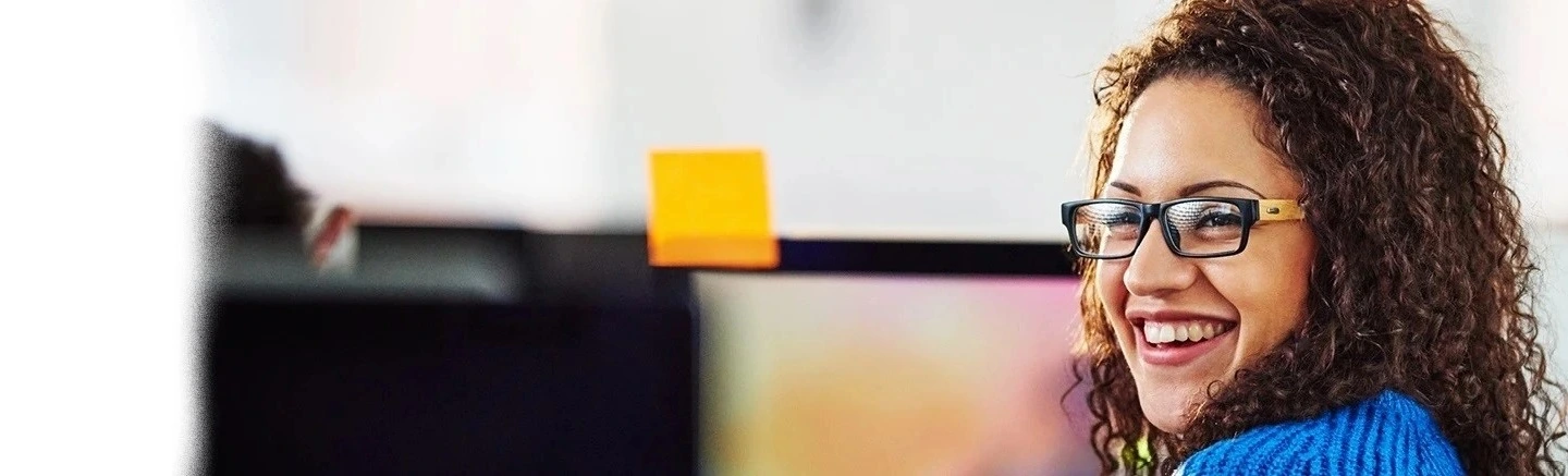 Person in a blue sweater working at a computer screen with a sticky note attached, showing a home workspace for effective job hunting and expert strategies to search smarter.