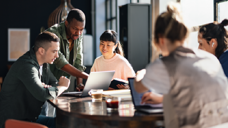 Team meeting around a table with laptops, discussing management strategies in a modern office.