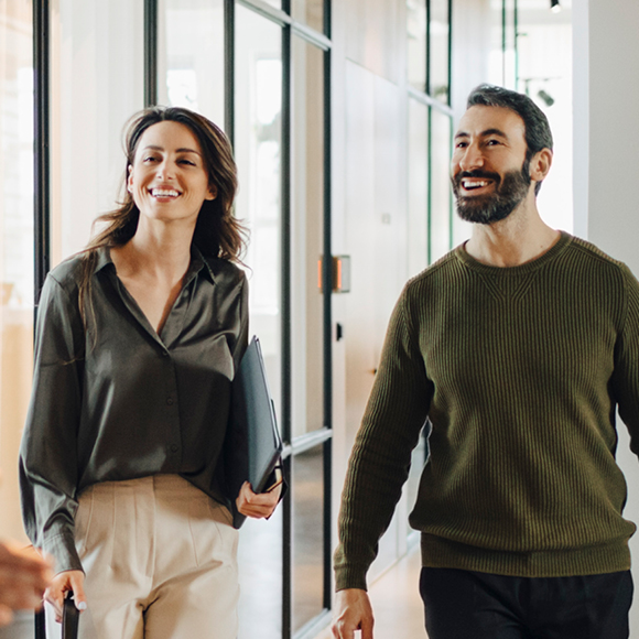 Two professionals walking through a modern office corridor, one carrying a laptop, representing jobseeker career hub resources.